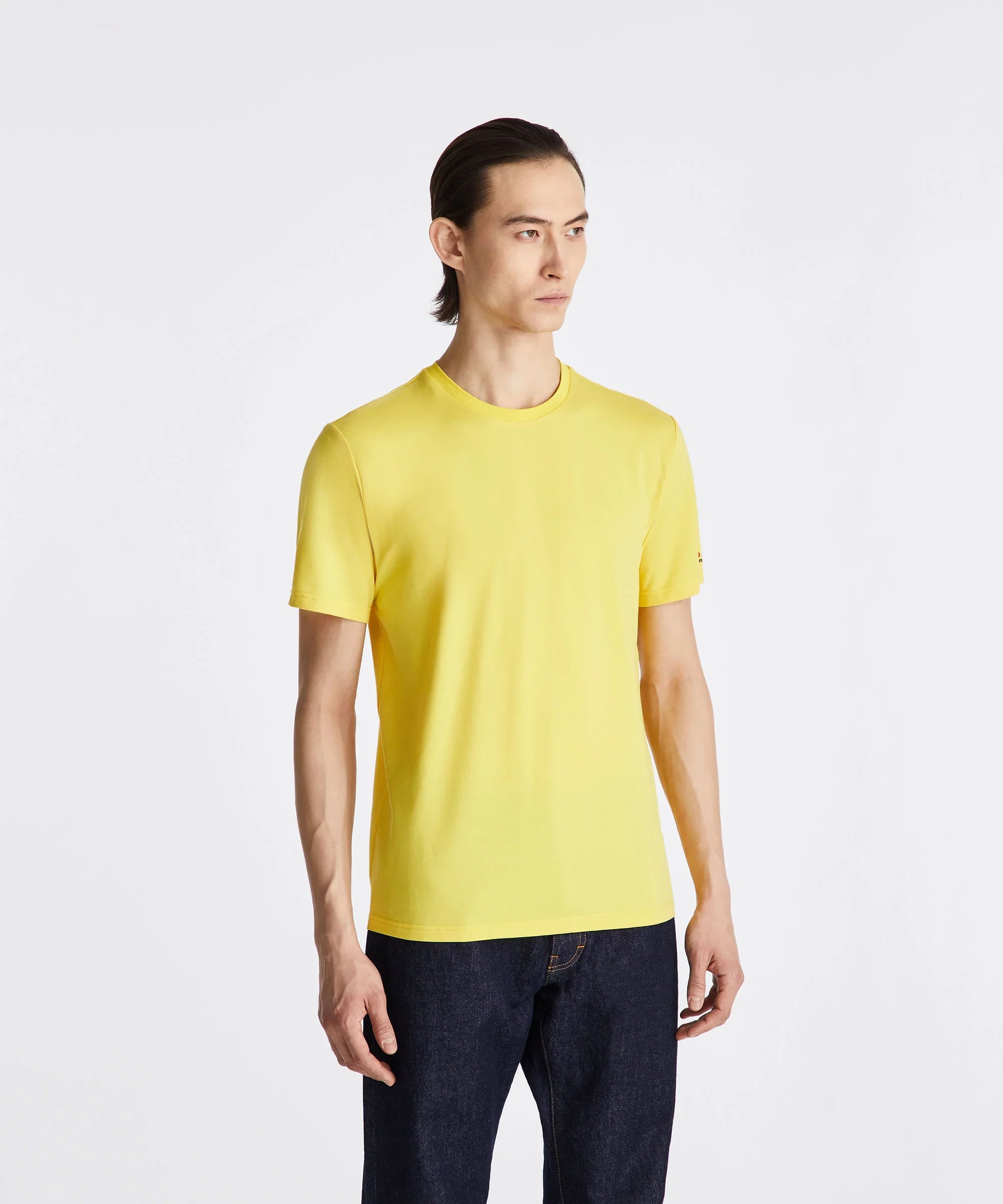 Uomo con t-shirt gialla a manica corta e jeans blu, sfondo bianco, moda casual.