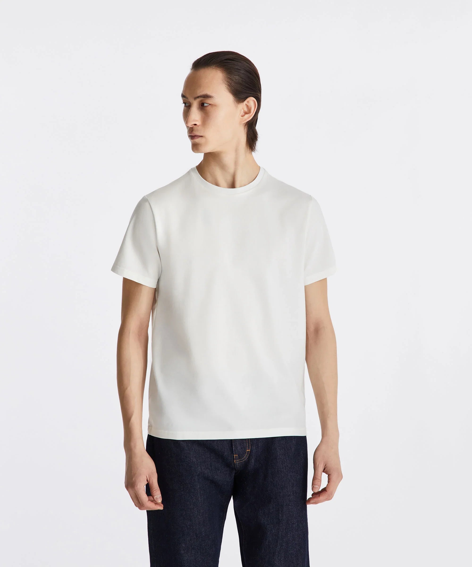 Modello uomo indossa t-shirt bianca basic abbinata a jeans blu, sfondo neutro.