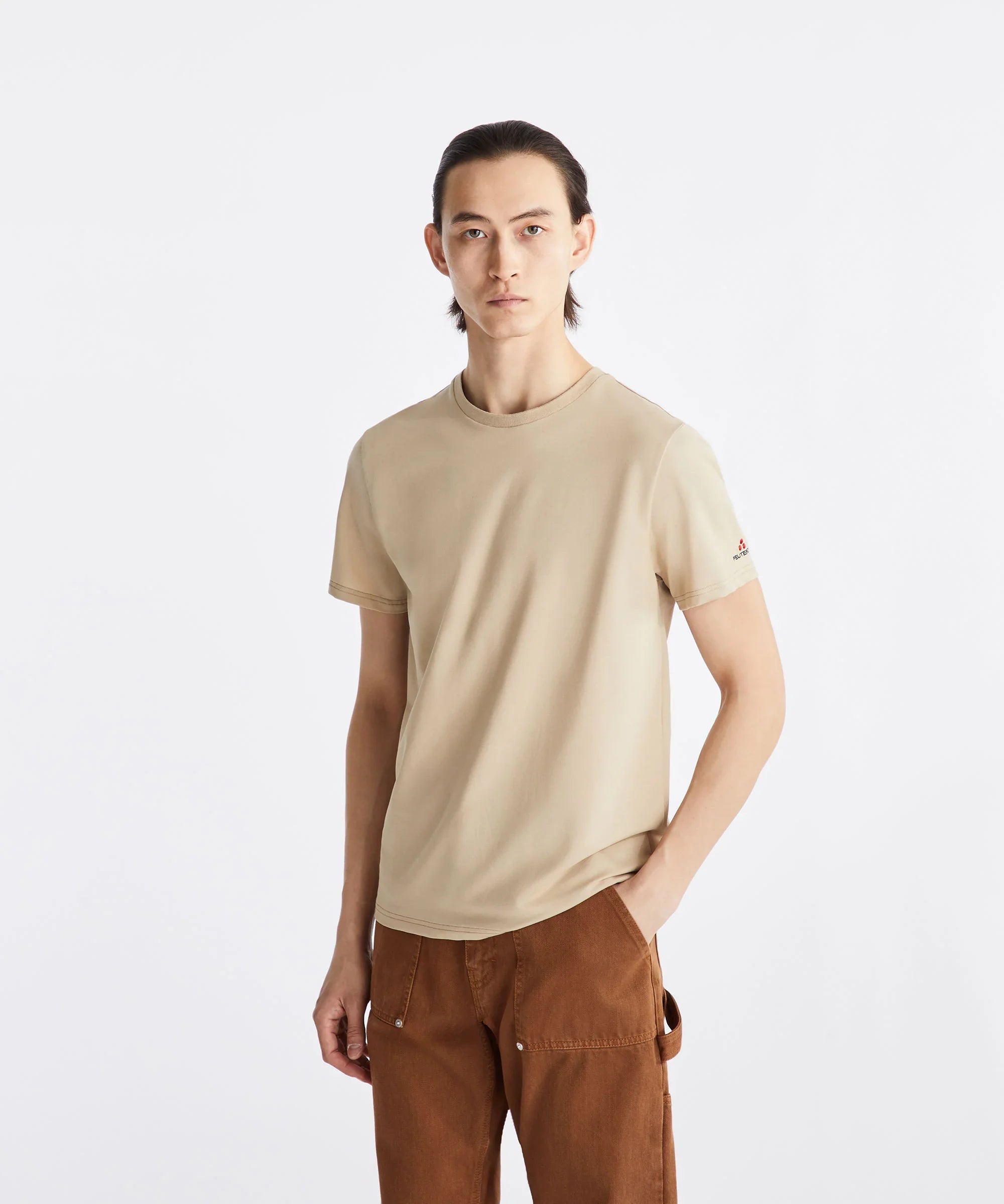 Modello uomo con t-shirt beige Peuterey e pantaloni marroni, sfondo bianco, moda casual
