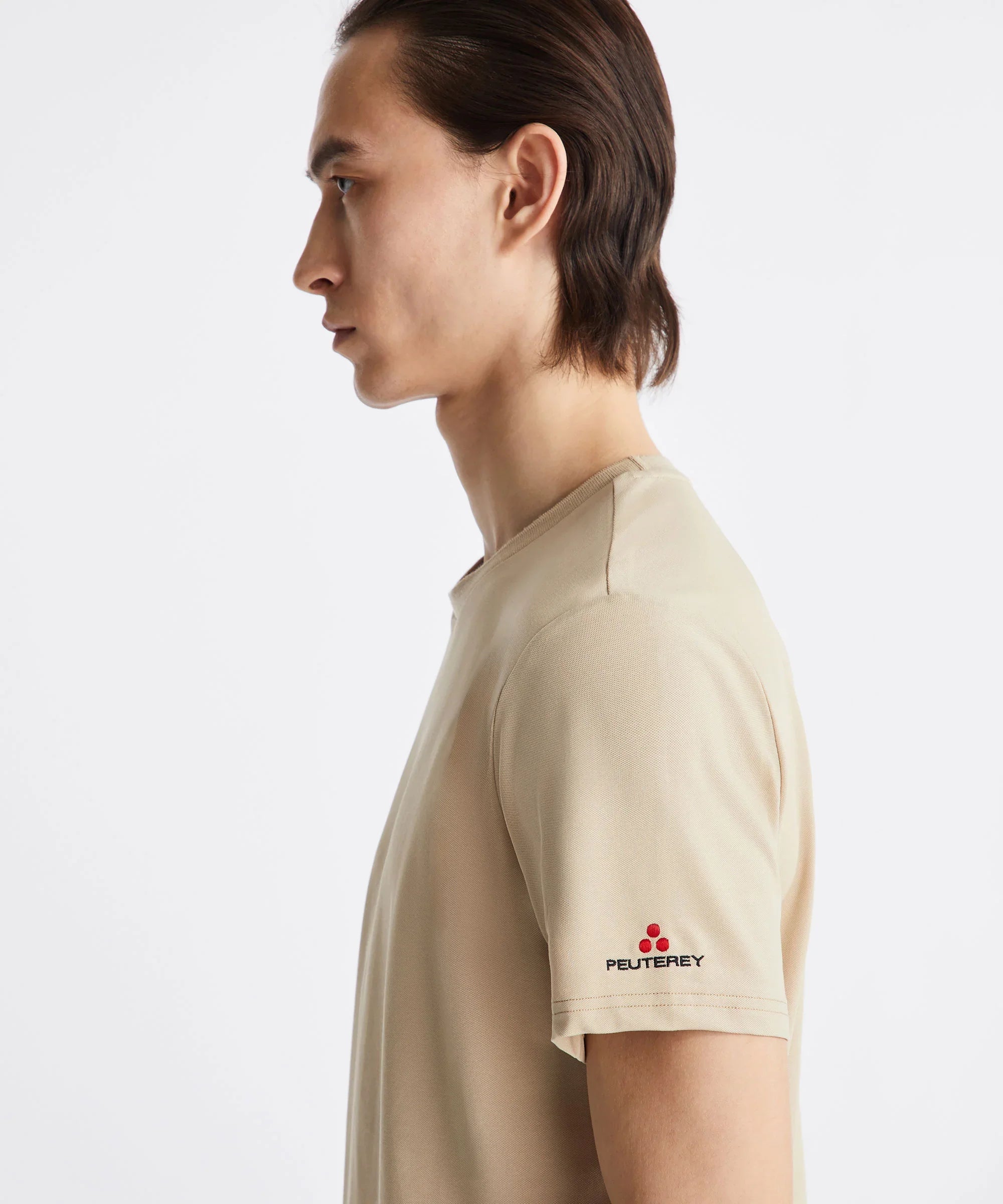 Uomo di profilo con t-shirt beige Peuterey, logo ricamato su manica, sfondo bianco