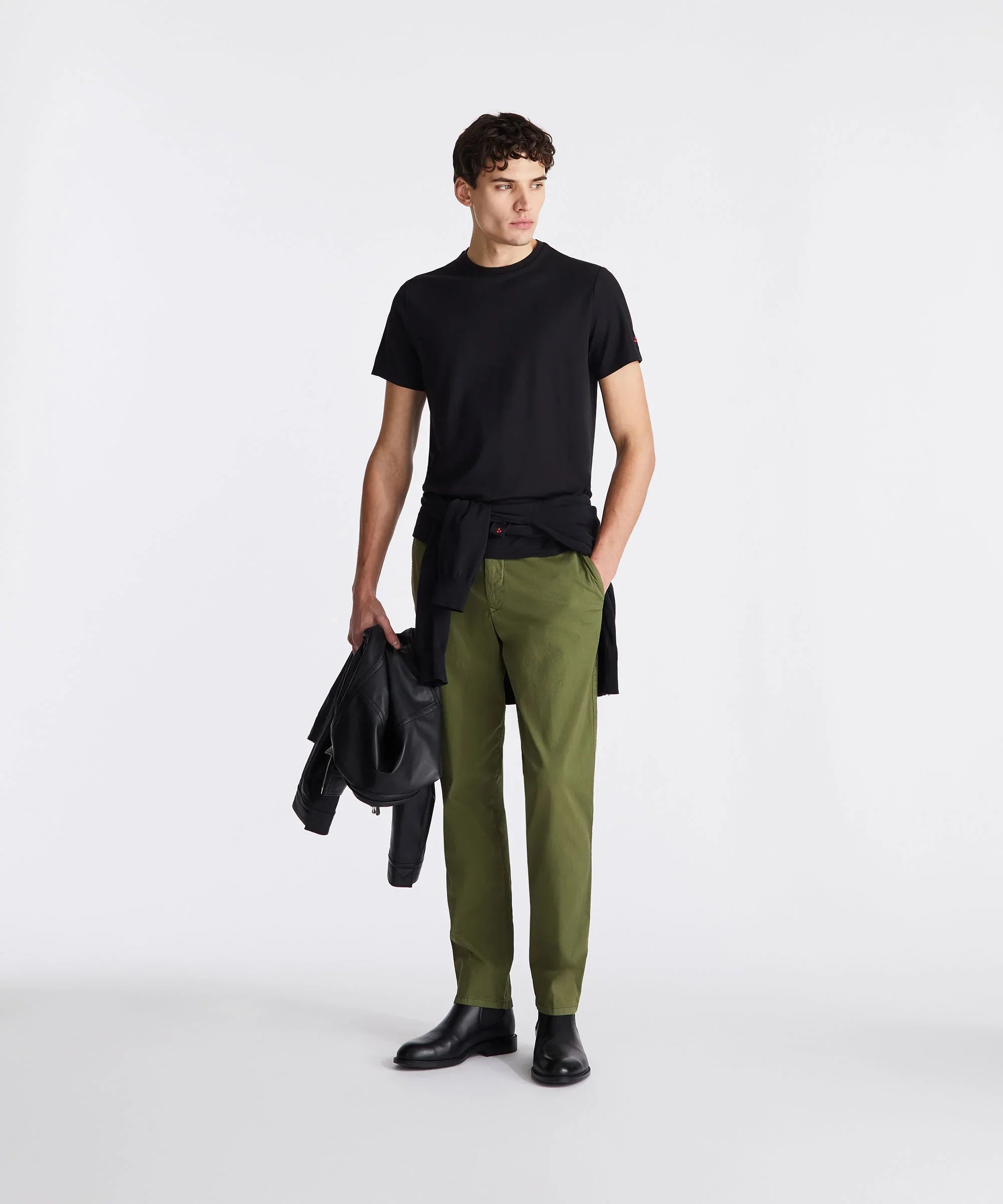 Modello uomo con t-shirt nera, pantaloni verdi, giacca nera e stivali eleganti