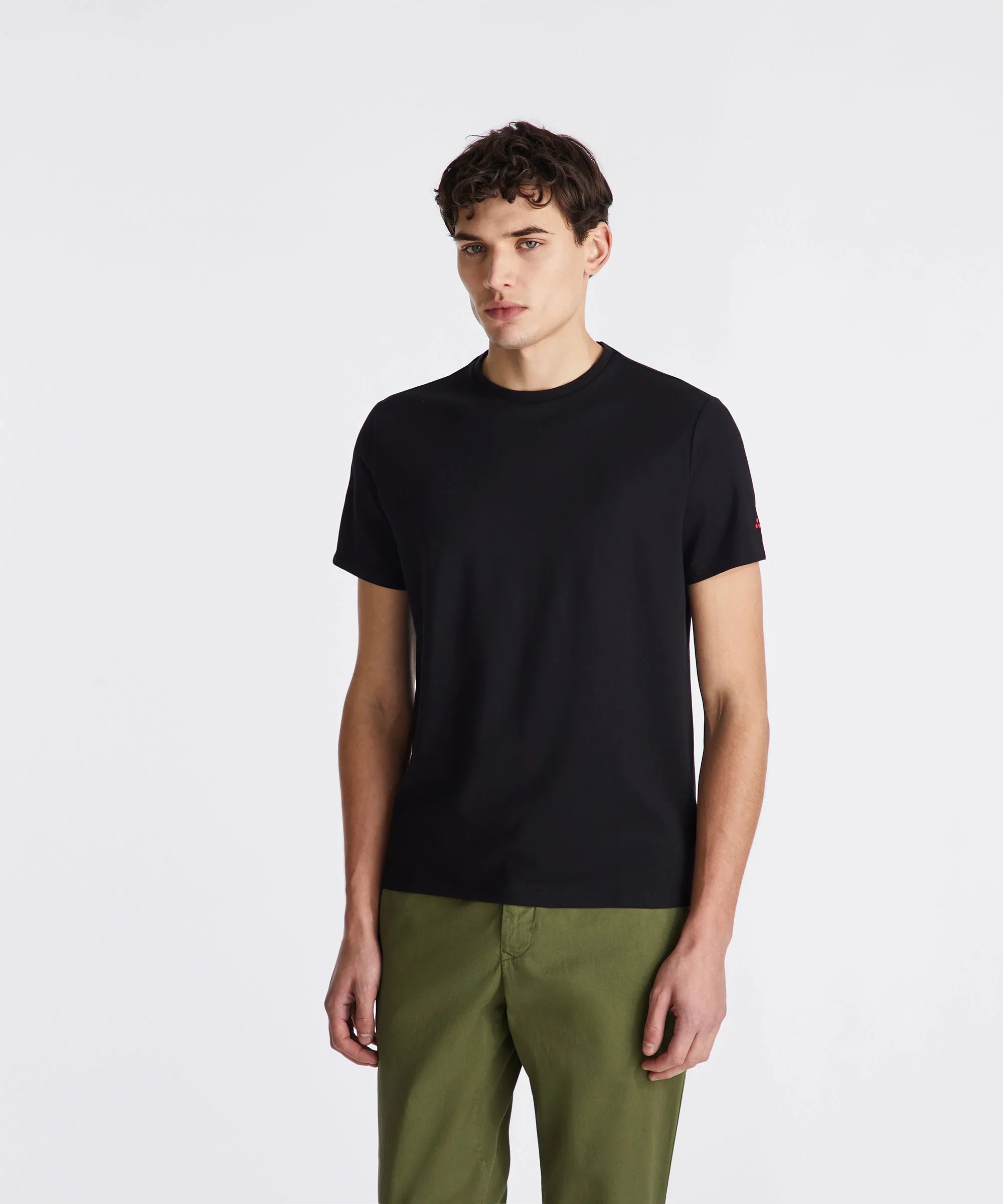 Modello uomo con t-shirt nera a manica corta e pantaloni verdi, sfondo bianco, moda casual.