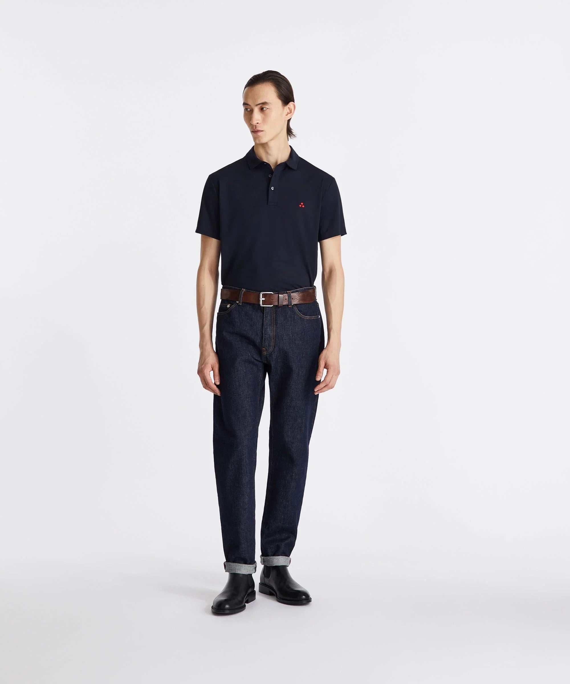 Modello uomo con polo blu scuro, jeans denim e stivaletti neri, look casual moda uomo.