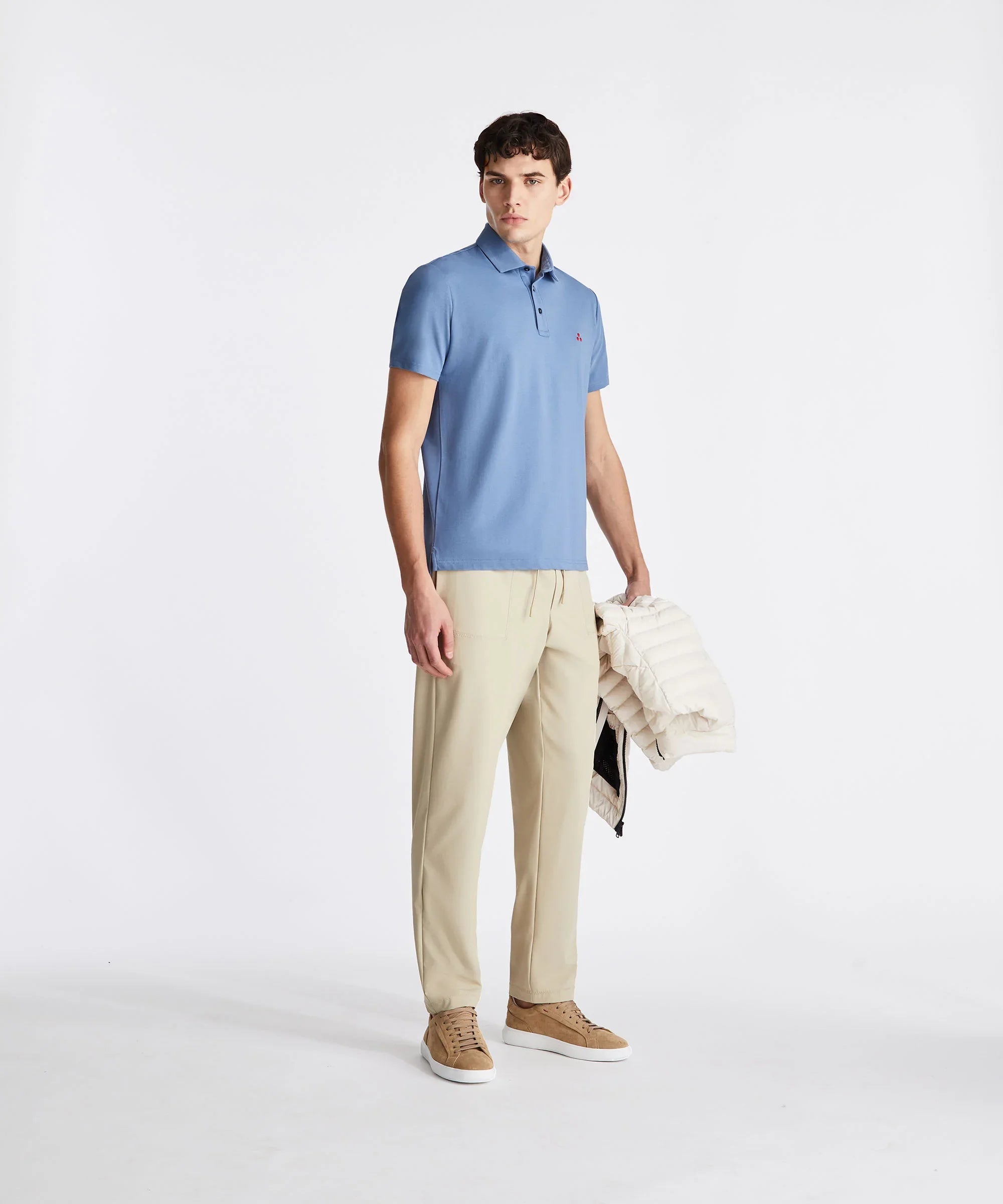 Modello uomo con polo azzurra, pantaloni beige, sneakers marroni e giacca trapuntata chiara