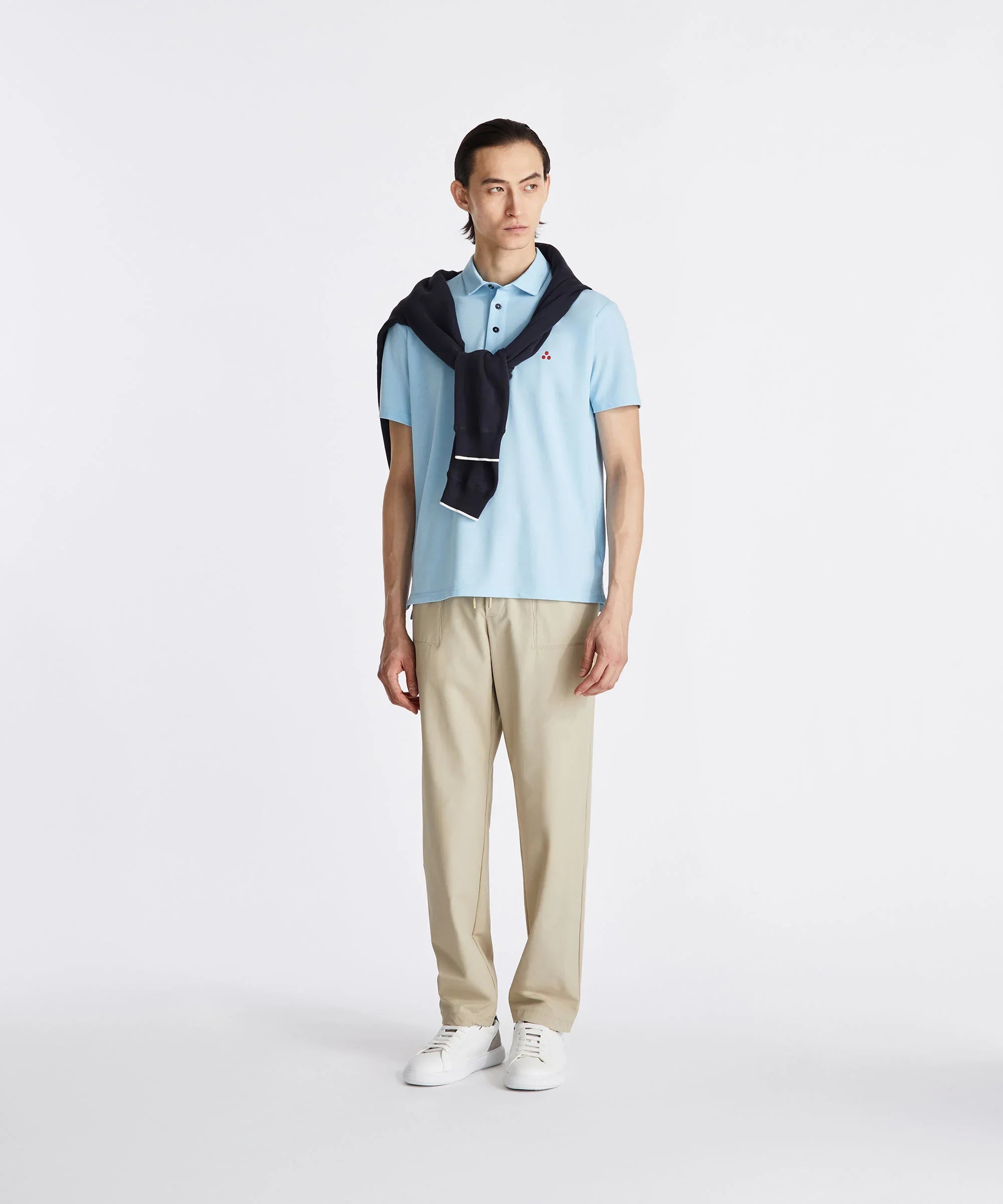 Modello uomo con polo celeste, pantaloni beige, sneakers bianche e maglia blu sulle spalle