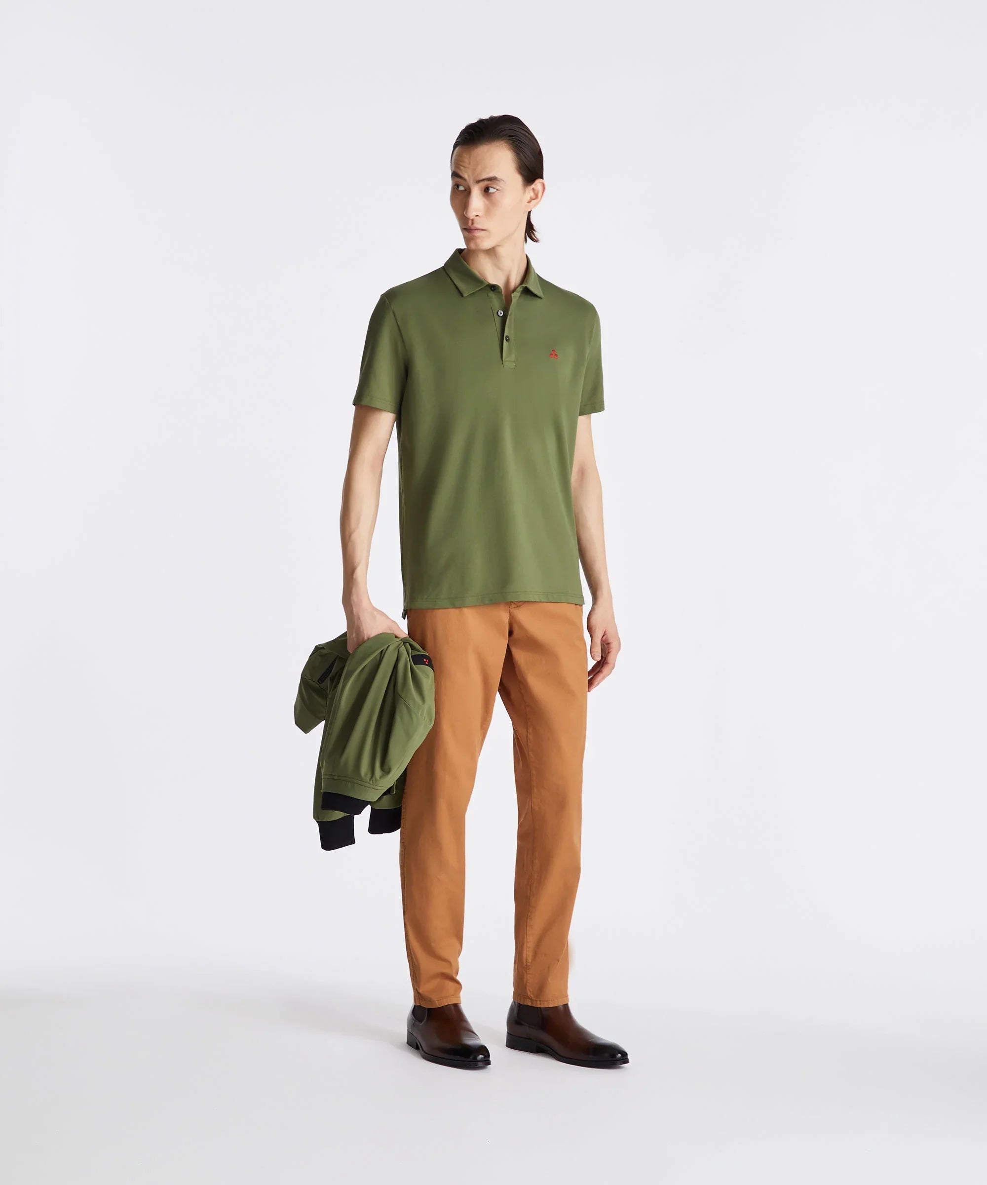 Modello uomo con polo verde oliva, pantaloni color ruggine e giacca abbinata in mano