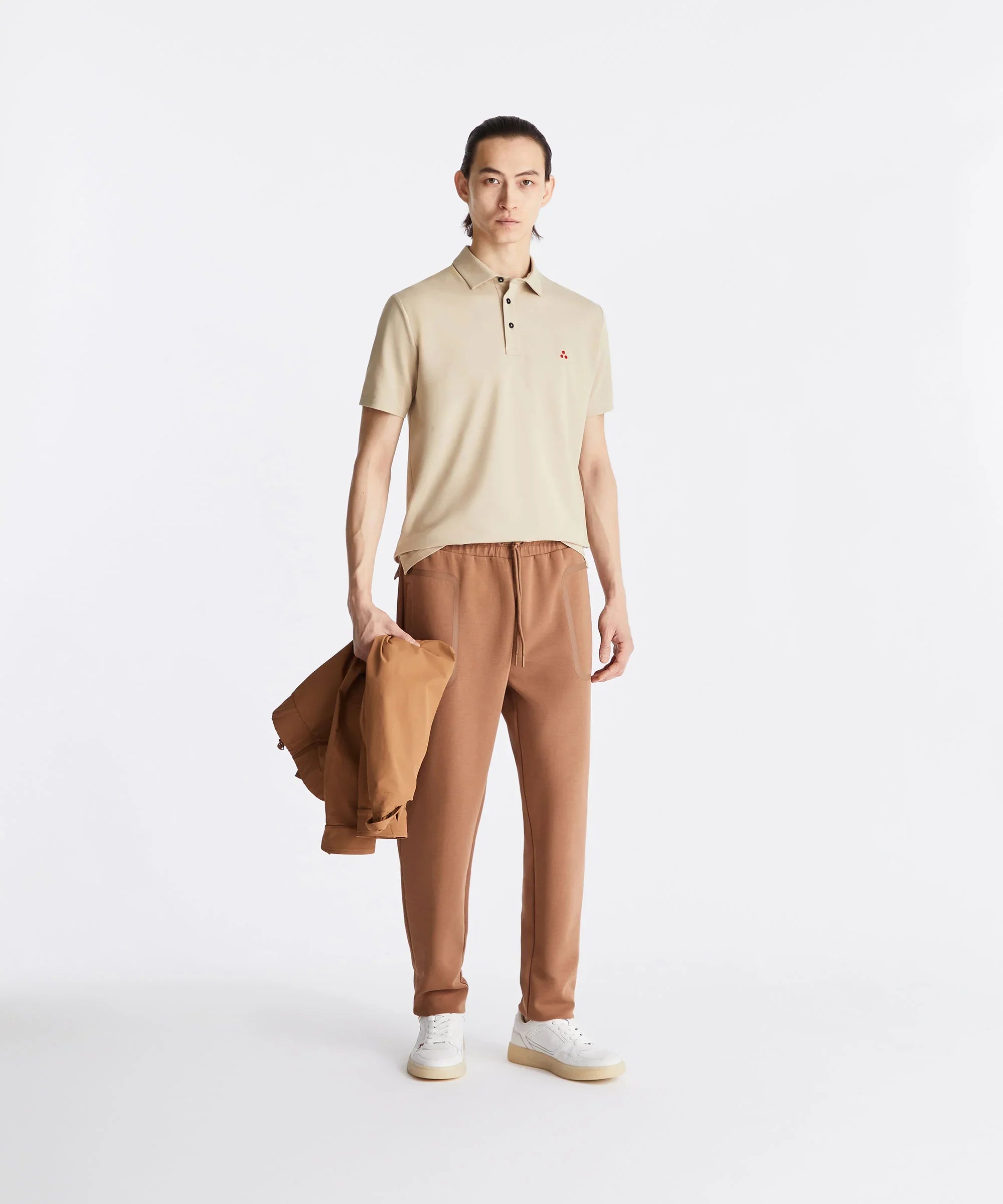 Modello con polo beige, pantaloni marroni e sneakers bianche, moda uomo casual elegante.
