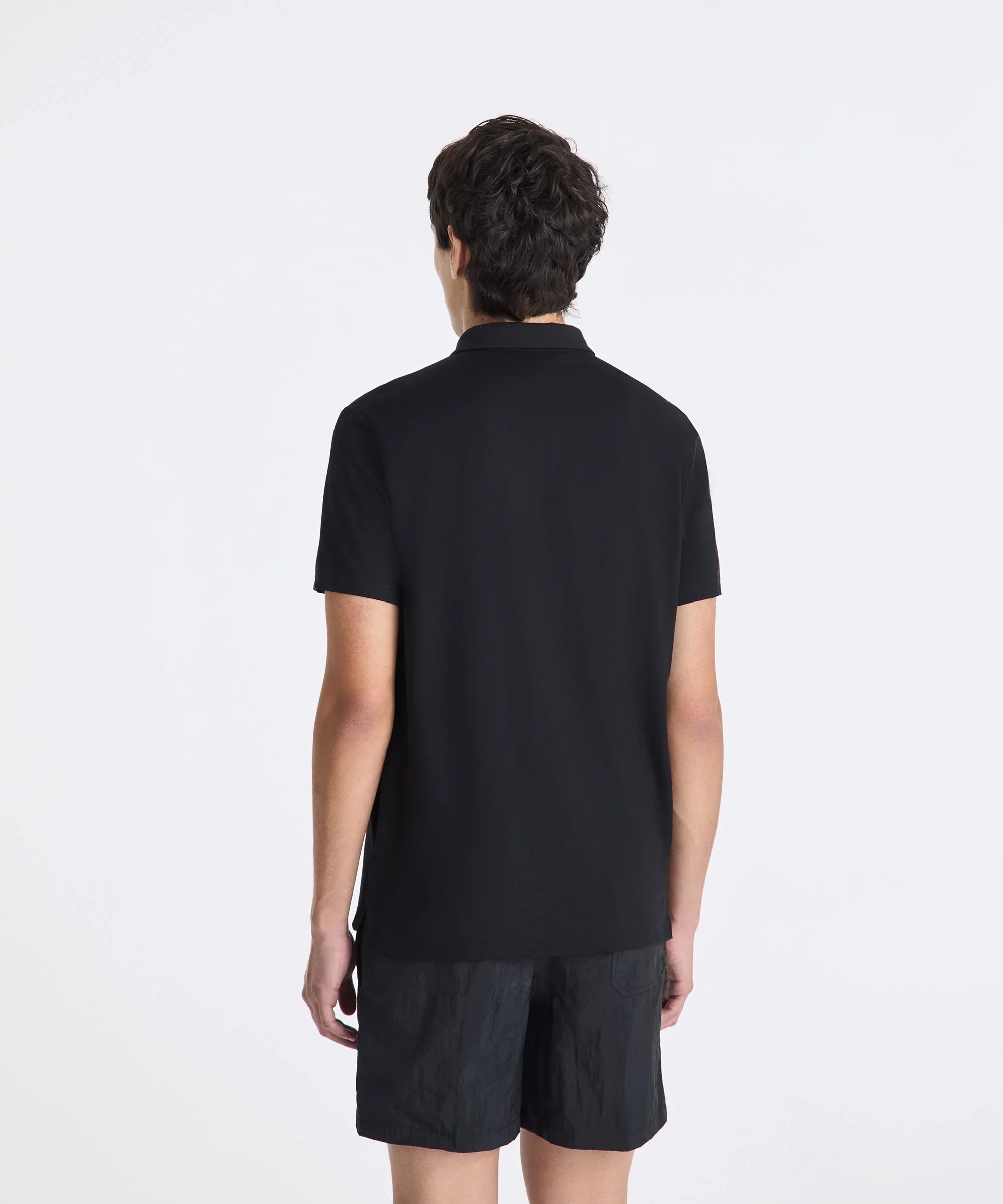 uomo di spalle con polo nera e pantaloncini neri, moda uomo casual