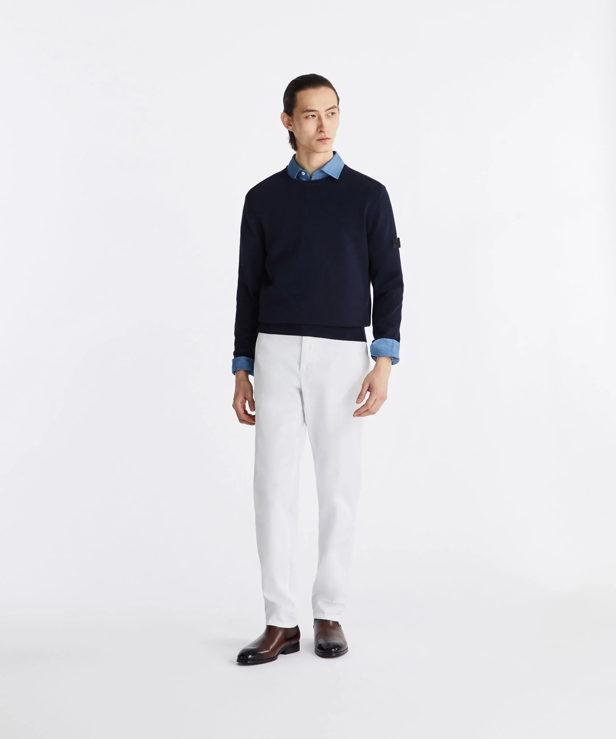 Modello indossa maglione blu, camicia azzurra, pantaloni bianchi e stivaletti uomo eleganti.