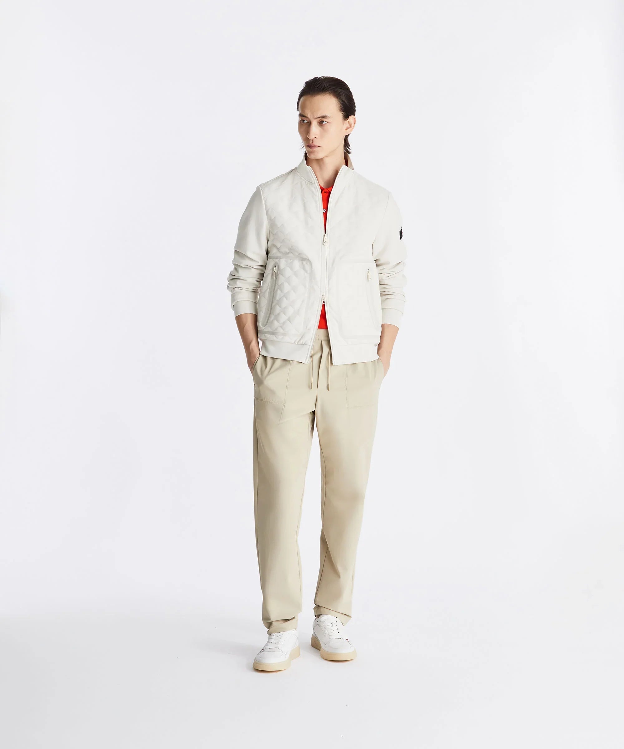 Modello uomo con giacca trapuntata bianca, pantaloni beige e sneakers bianche, su sfondo neutro