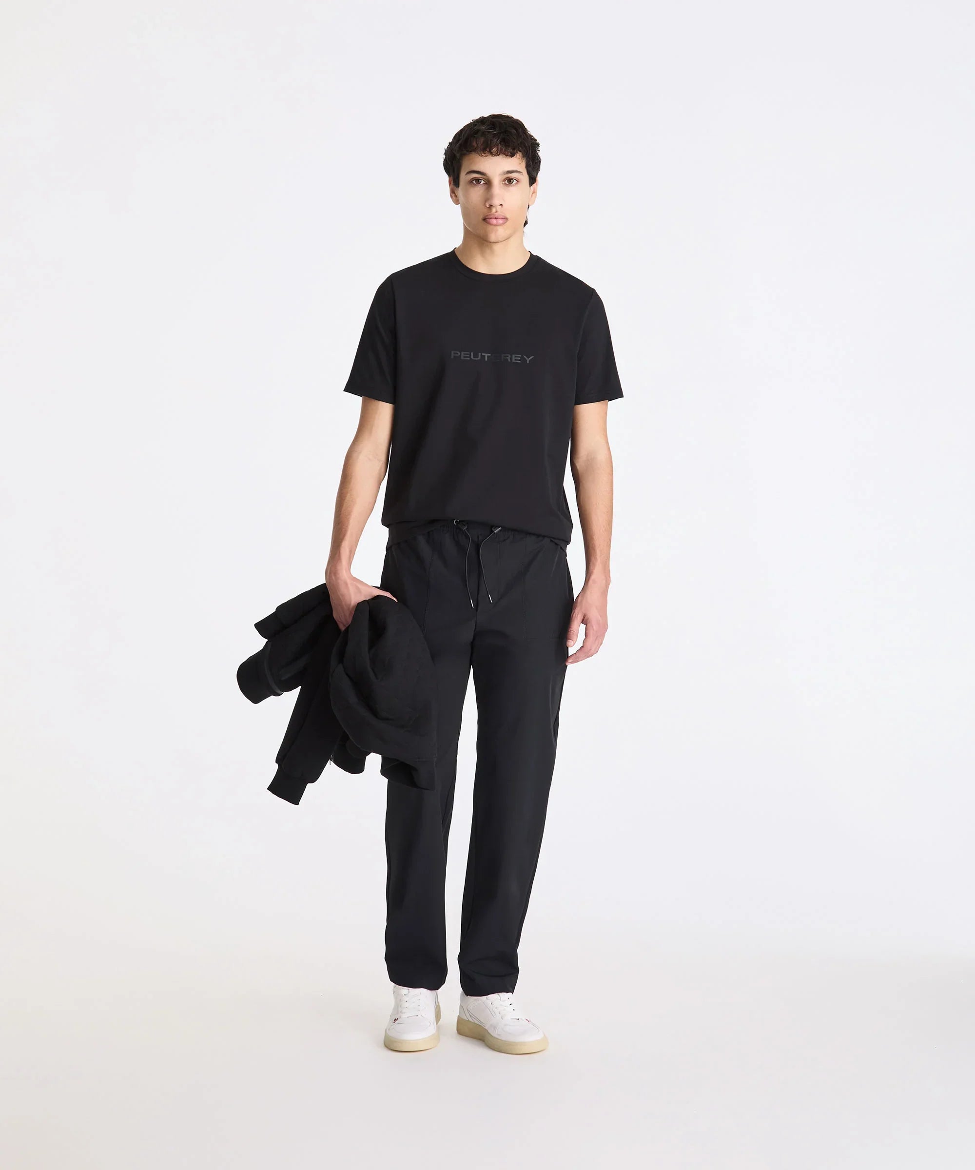 Modello uomo con t-shirt Peuterey nera, pantaloni eleganti neri e sneakers bianche