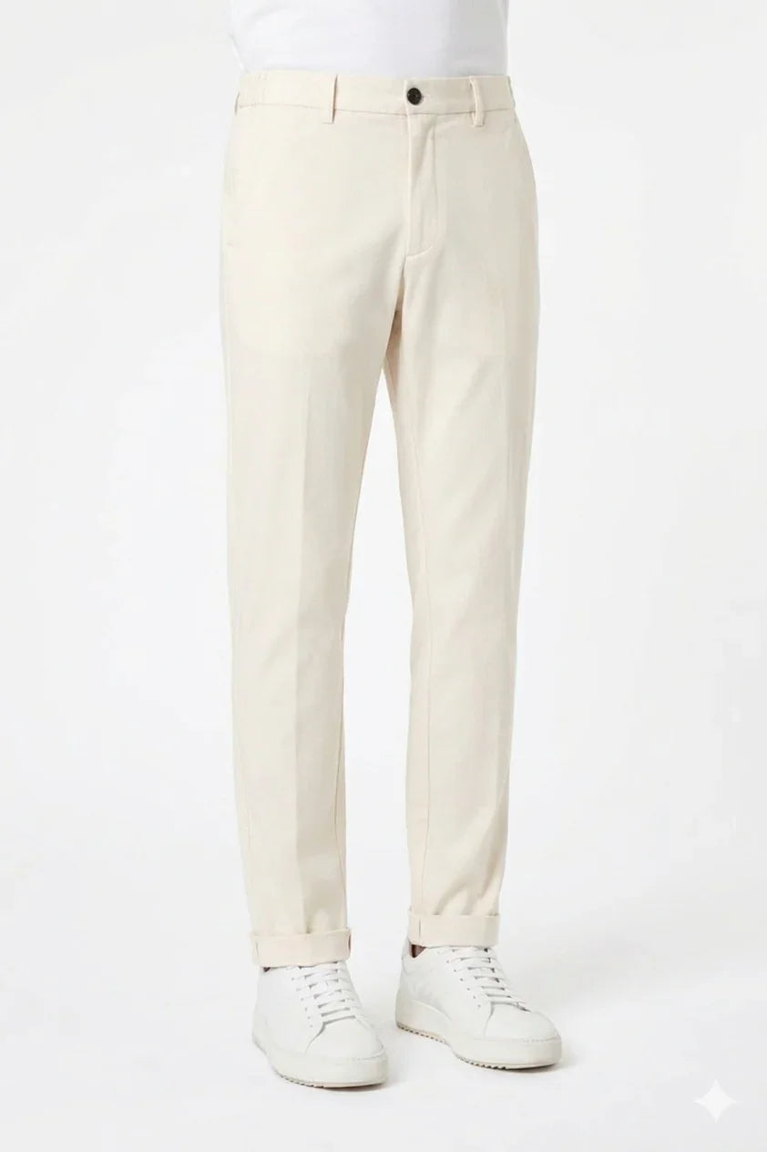 Pantaloni uomo beige eleganti, risvoltati, abbinati a sneakers bianche su sfondo neutro