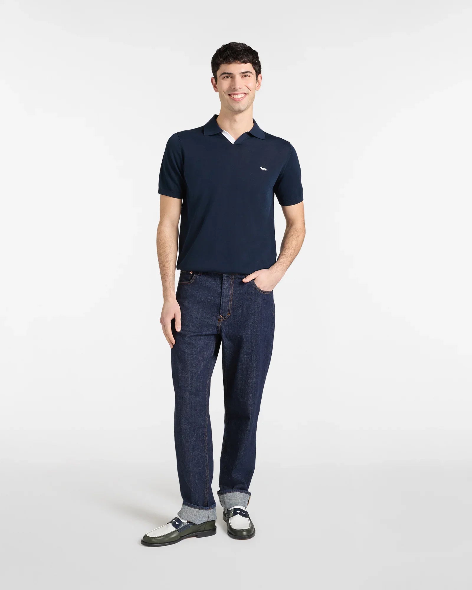 Uomo con polo blu a maniche corte, jeans scuri e mocassini bicolore, stile casual elegante