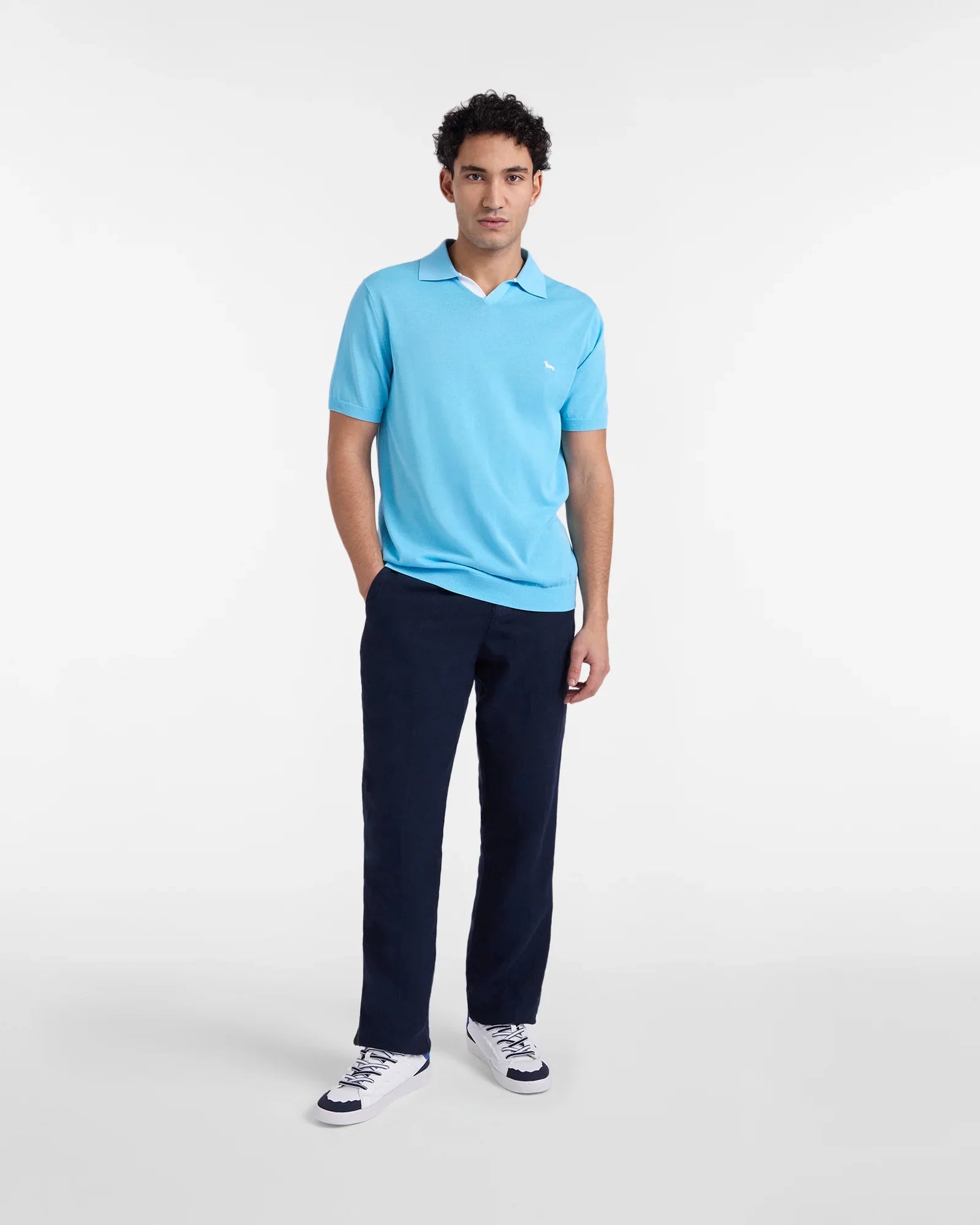 Modello indossa polo azzurra a maniche corte, pantaloni blu e sneakers bianche uomo.