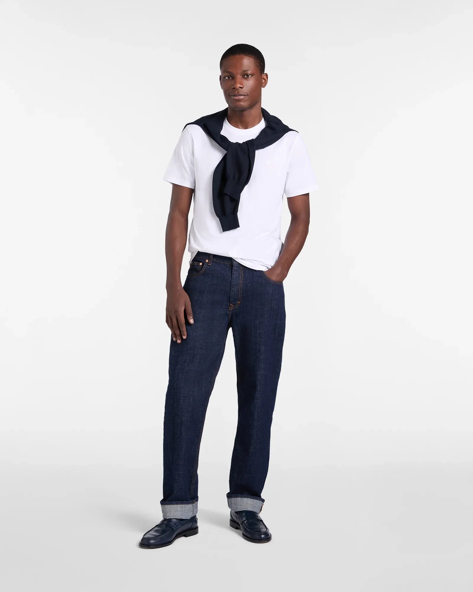 Modello indossa t-shirt bianca, jeans blu scuro con risvolto e mocassini eleganti uomo.