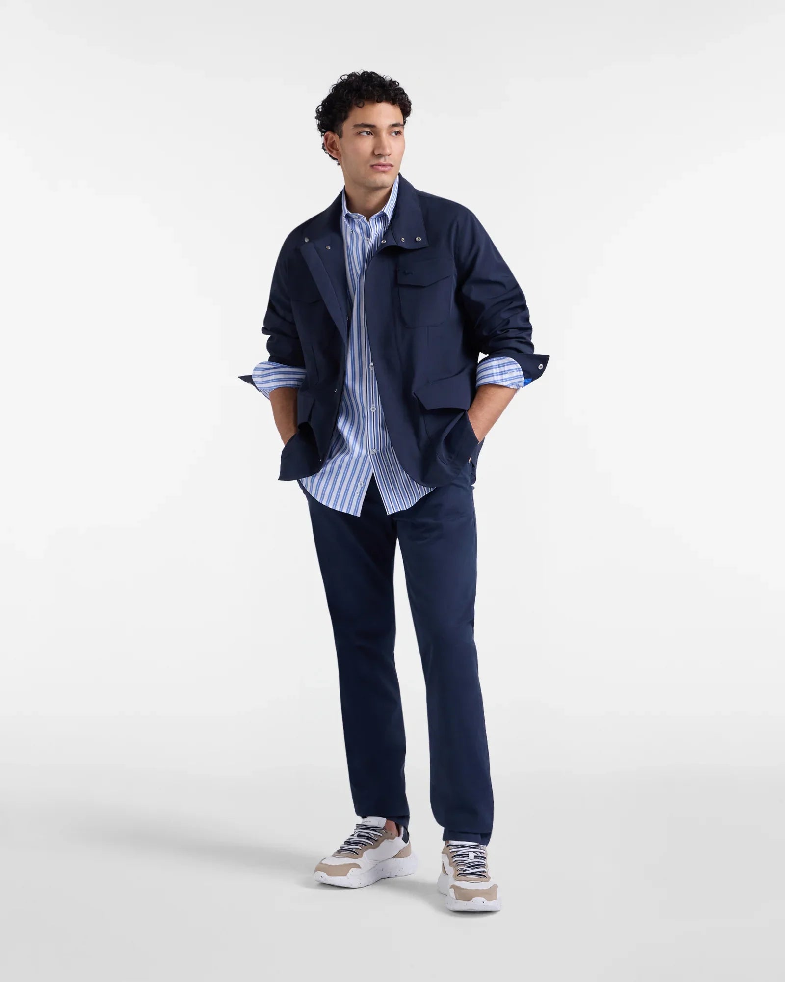 Uomo con giacca blu, camicia a righe azzurre e pantaloni blu, look casual elegante.