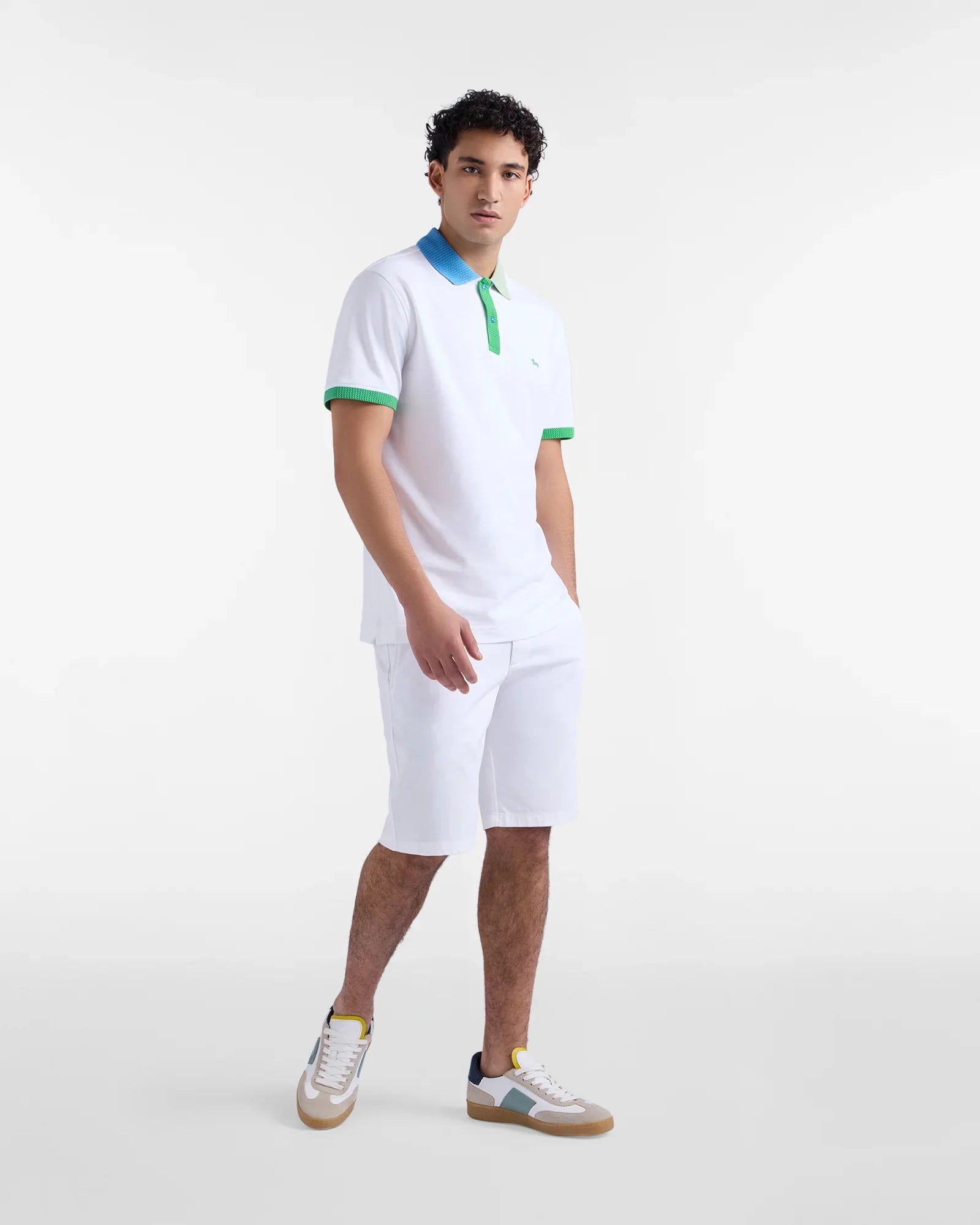 Modello uomo con polo bianca dettagli verde e blu, bermuda bianchi e sneakers alla moda