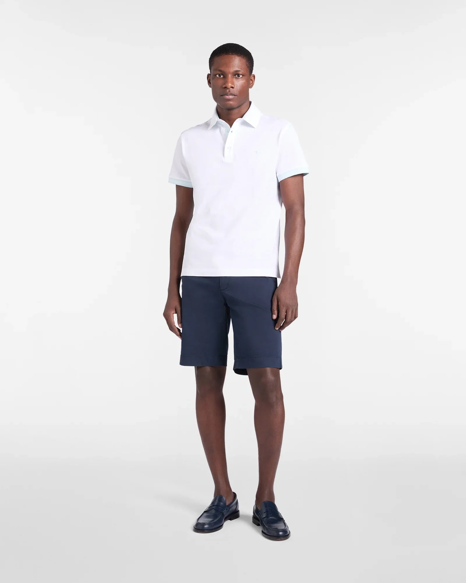 Uomo con polo bianca, bermuda blu e mocassini in pelle, abbigliamento estivo elegante.