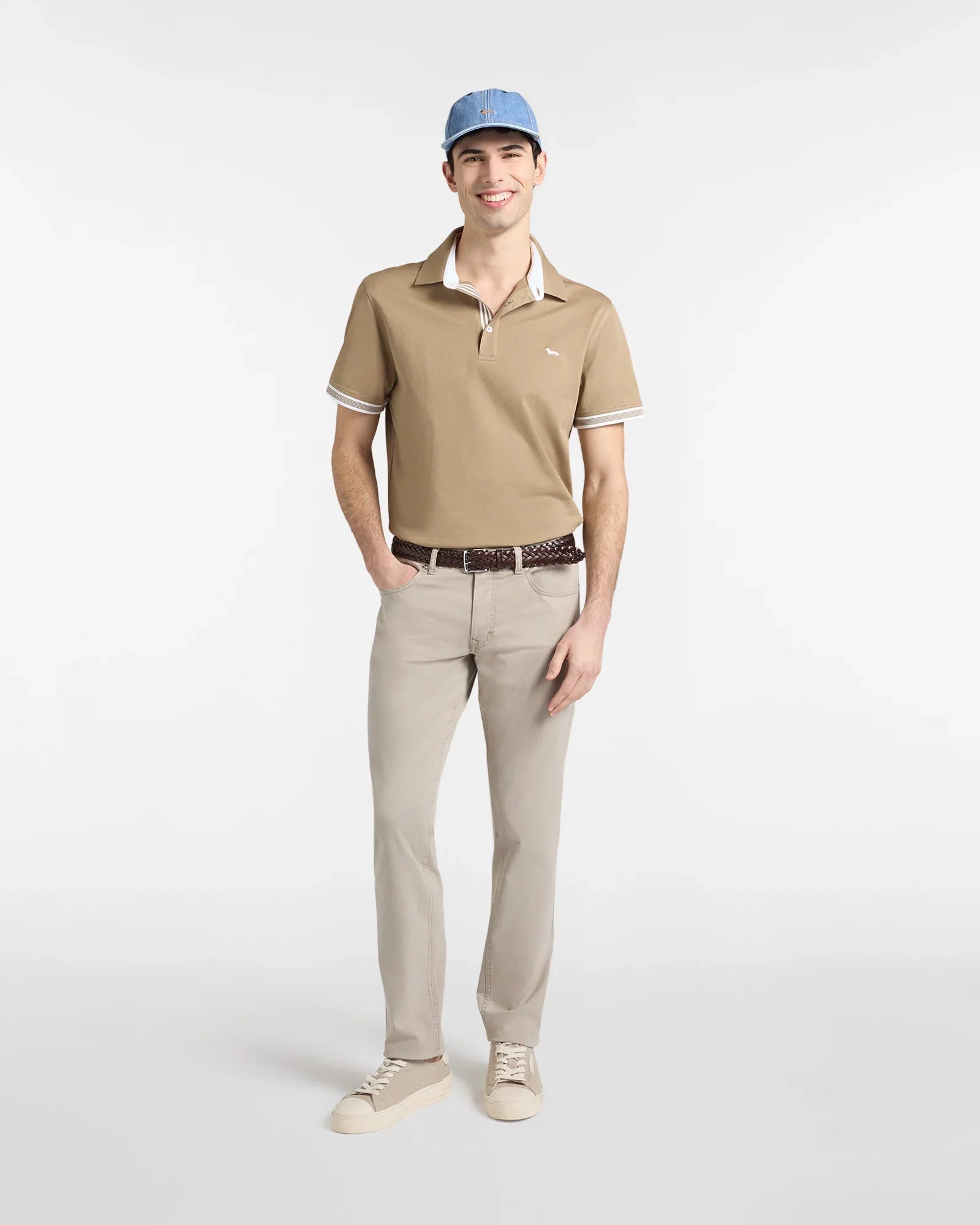 Uomo con polo beige, pantaloni chiari, cappellino azzurro e sneakers, moda casual uomo