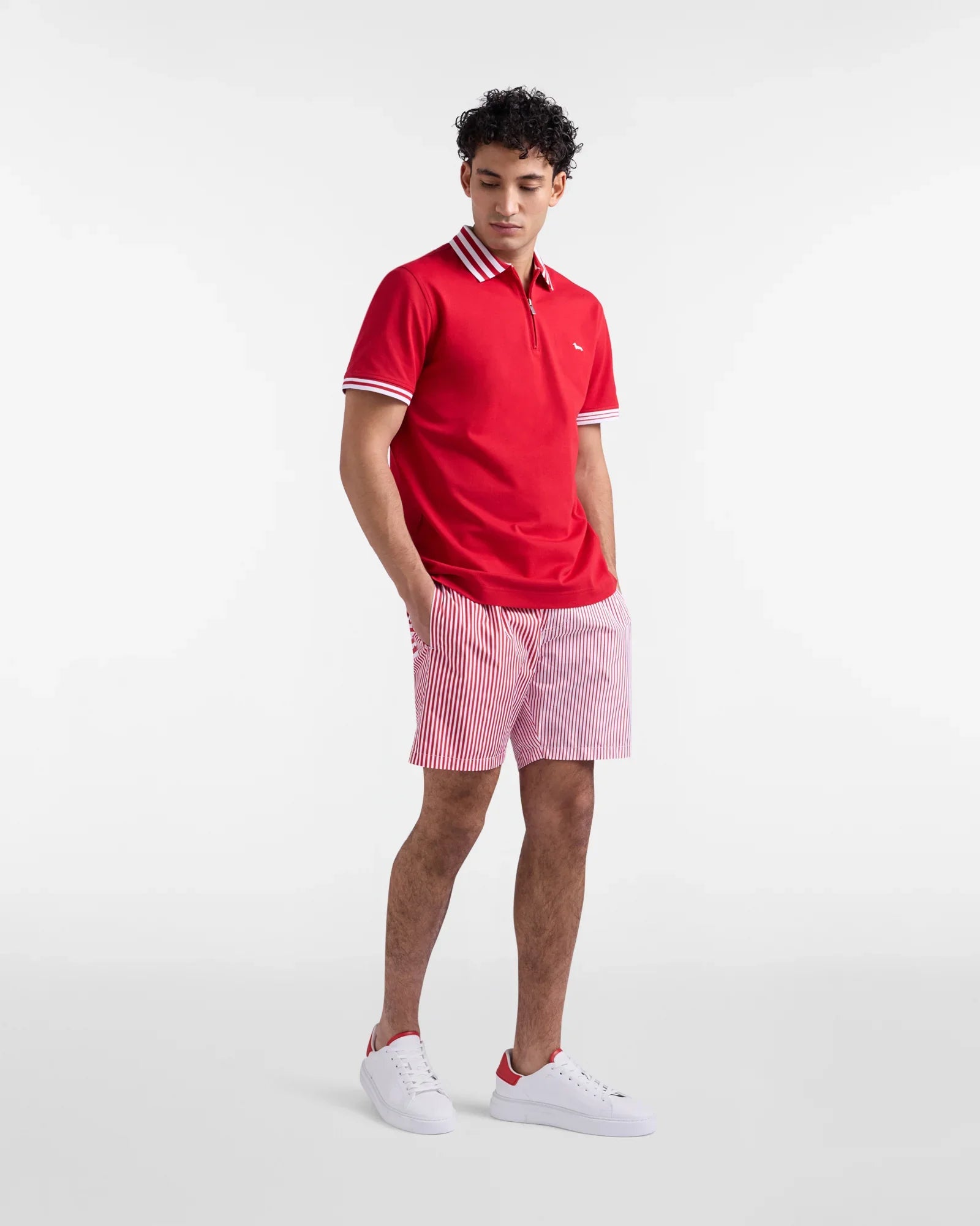 Modello uomo con polo rossa, pantaloncini rigati bianchi e rossi, sneakers bianche