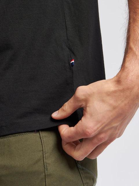 Dettaglio t-shirt nera uomo con mini etichetta tricolore, pantalone verde, stile casual