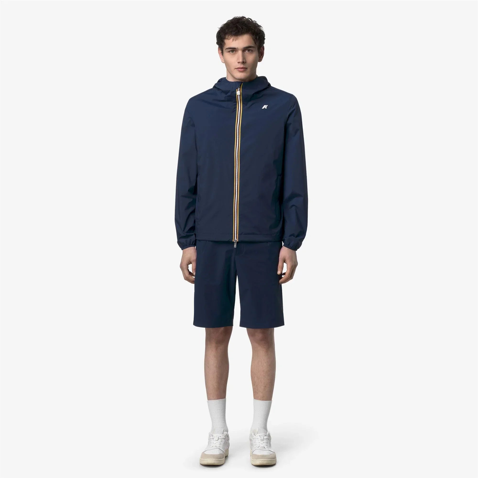 Modello uomo con giacca leggera blu con cappuccio e pantaloncini, look casual estivo