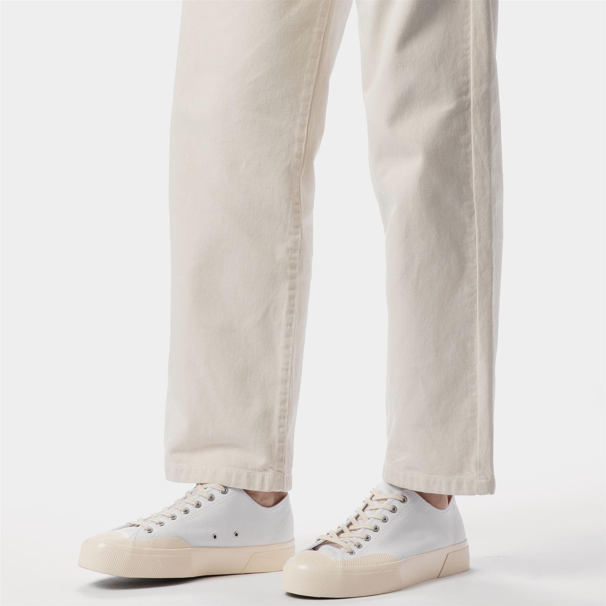 Sneakers bianche da uomo su fondo bianco, abbinate a pantaloni chiari in cotone.