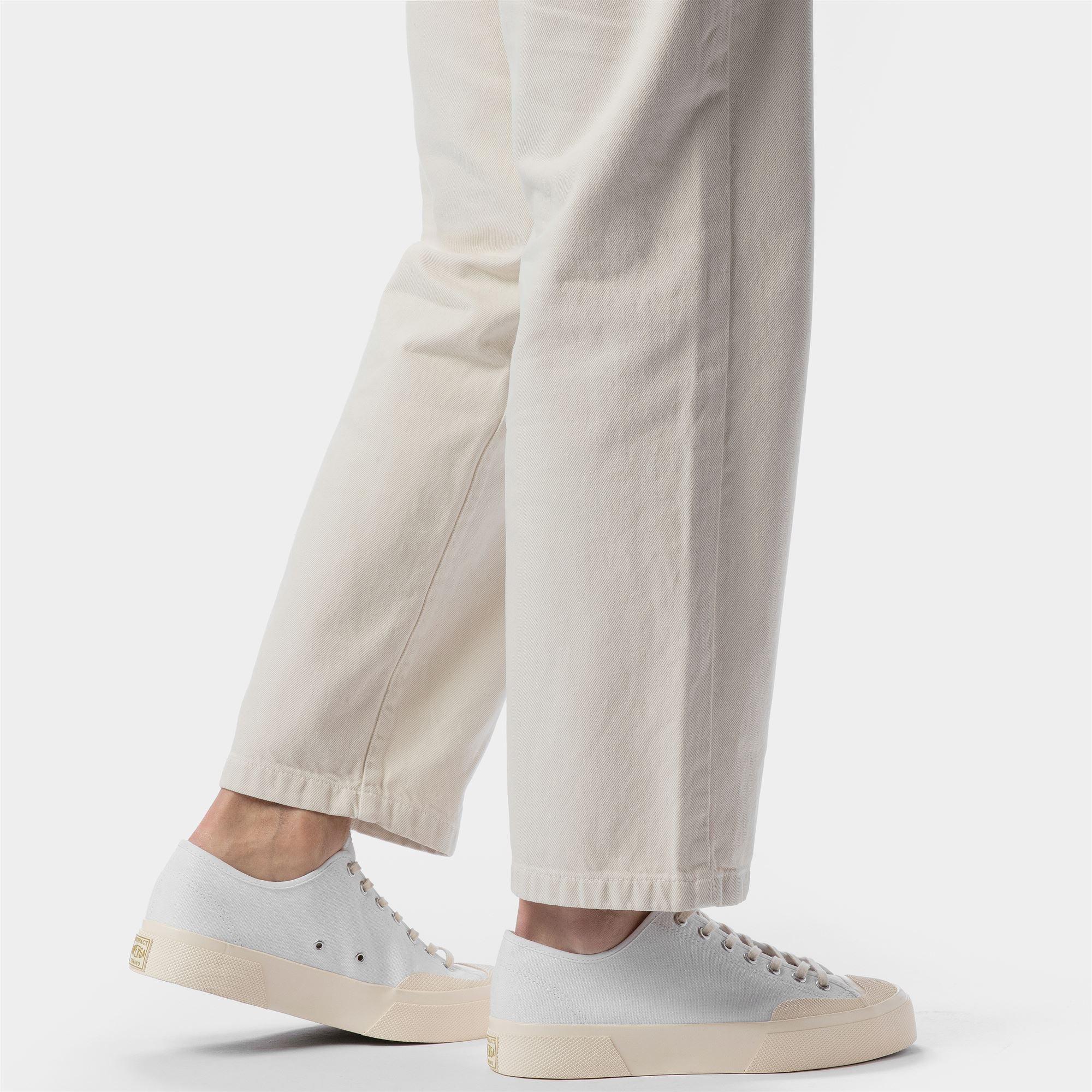 Sneakers bianche basse da uomo abbinate a pantaloni chiari, moda casual elegante