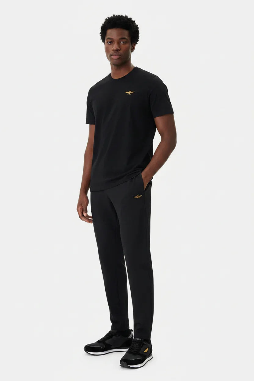 Modello indossa t-shirt nera regular fit uomo con logo dorato sul petto e pantaloni coordinati.