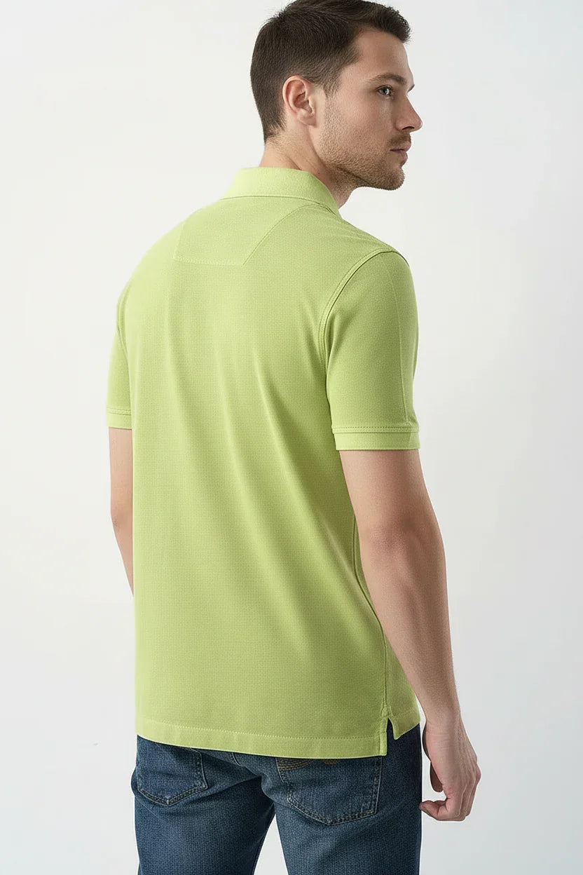 Uomo di profilo indossa polo verde chiaro a maniche corte e jeans, sfondo neutro