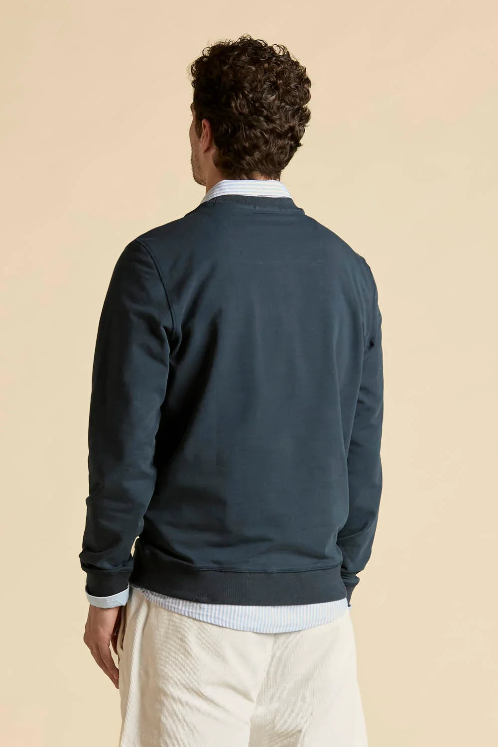 uomo di spalle con felpa blu girocollo, camicia celeste e pantaloni chiari, moda casual uomo