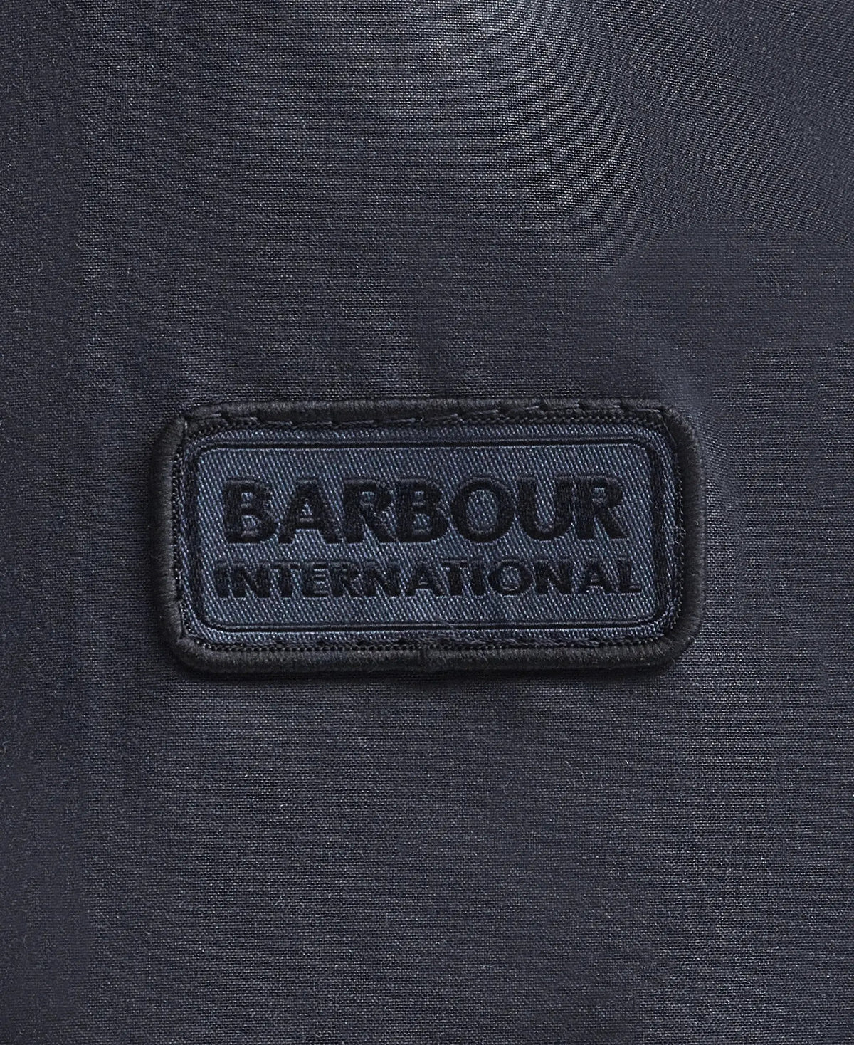 Dettaglio etichetta Barbour International su tessuto giacca cerata blu navy uomo