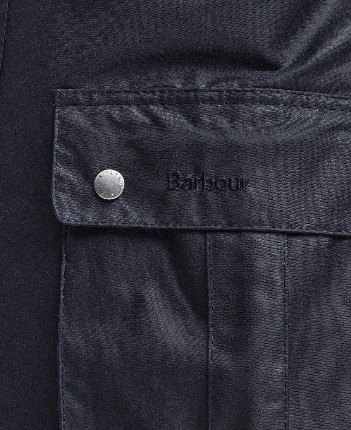dettaglio tasca giacca cerata blu navy con bottone metallico e logo Barbour ricamato