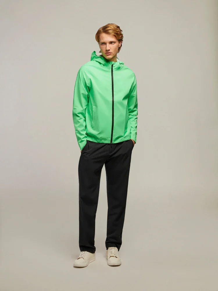 Modello uomo con giacca verde chiaro con cappuccio, pantaloni neri e sneakers bianche.