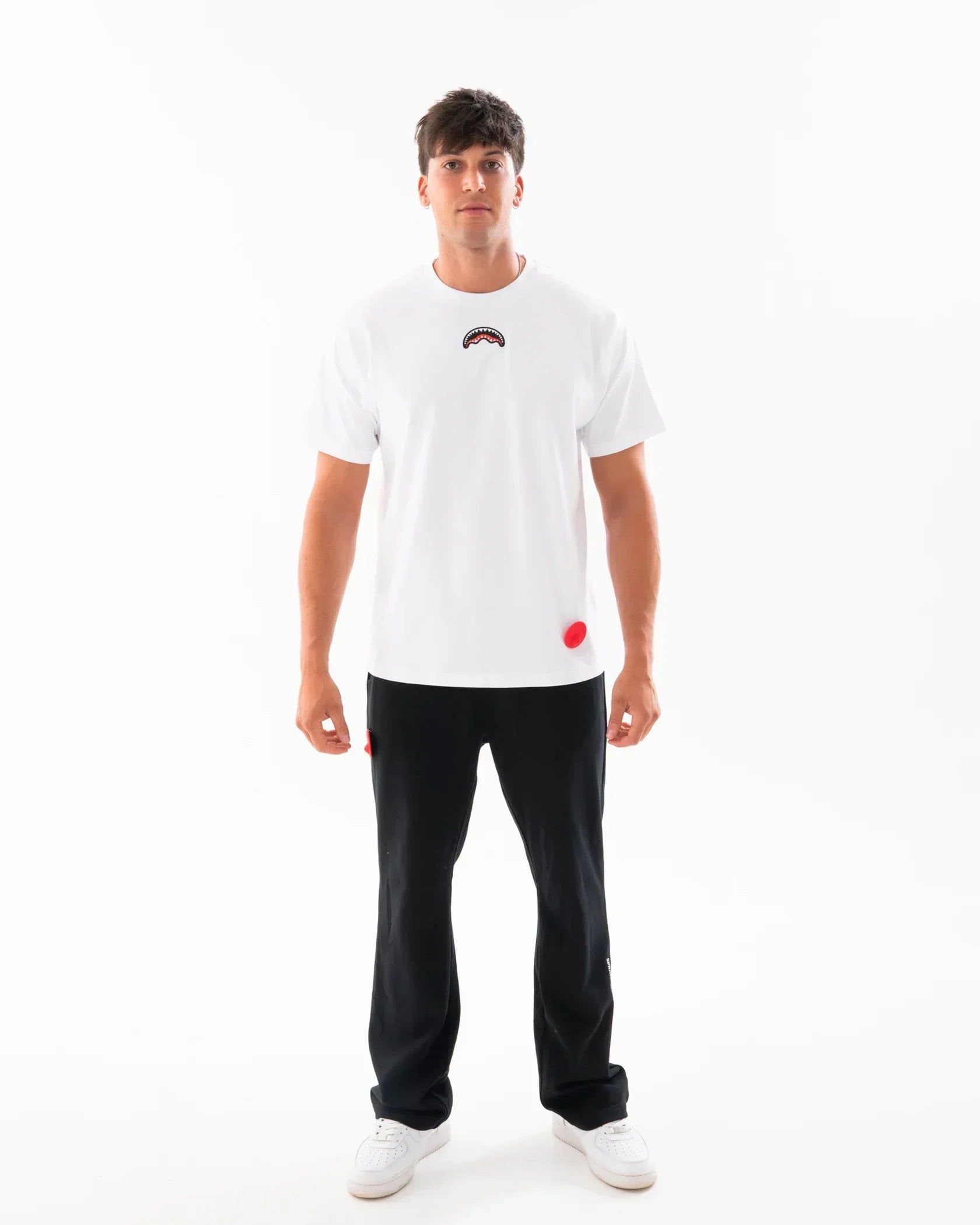 Modello con t-shirt bianca stampata, pantaloni neri e sneakers bianche su sfondo neutro