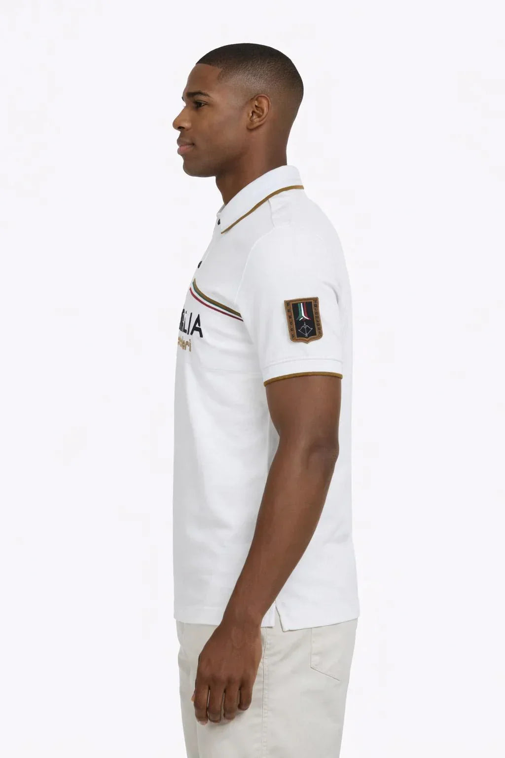 Uomo con polo bianca manica corta con dettagli dorati e patch sulla manica, stile casual elegante.