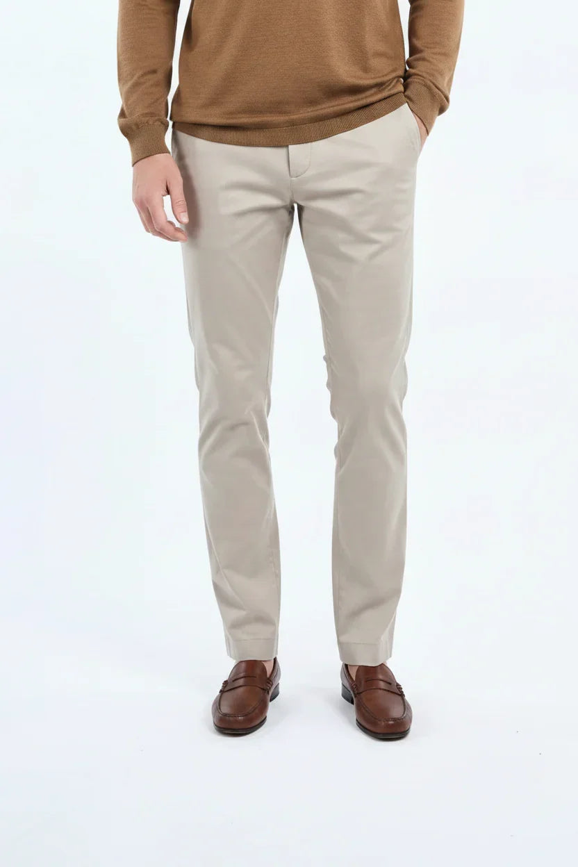 Pantaloni chino beige uomo eleganti, abbinati a maglione marrone e mocassini in pelle marrone.