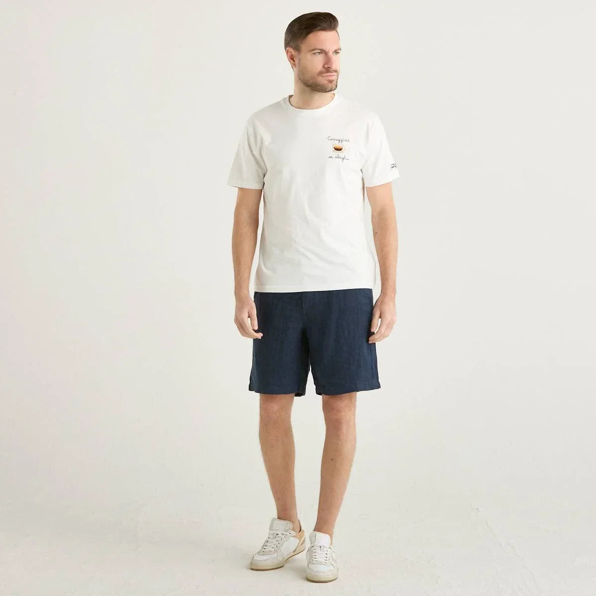 Modello indossa t-shirt bianca, bermuda blu navy e sneakers bianche, moda uomo casual.