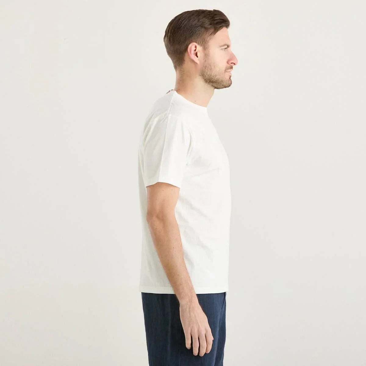 Uomo indossa t-shirt bianca basic e pantaloni blu, vista profilo, sfondo neutro